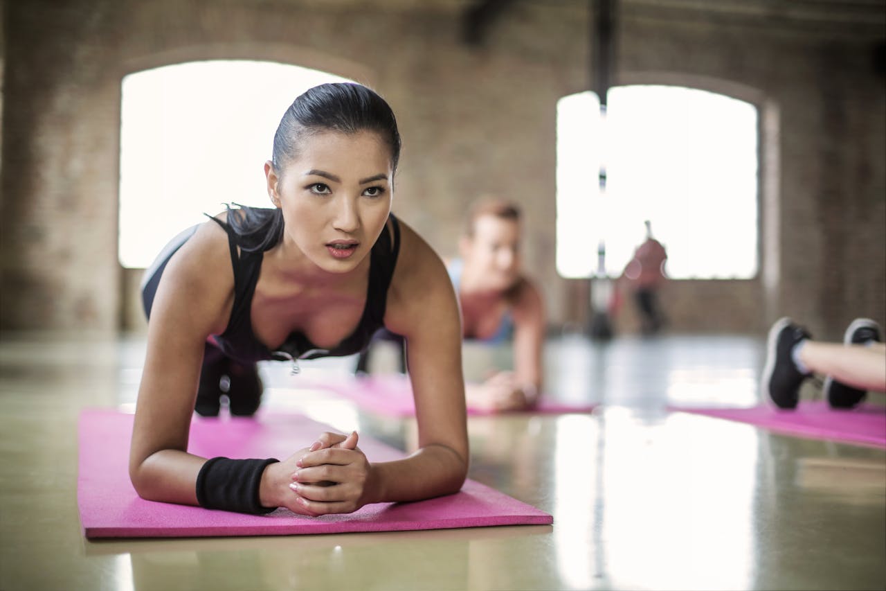 Two women engaging in a focused yoga session on pink mats in a spacious indoor studio.