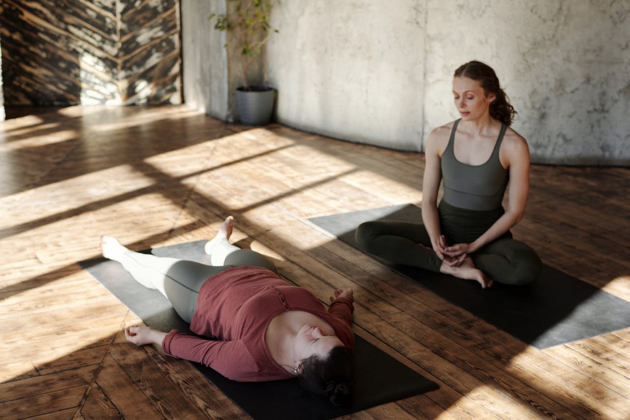 Two women practicing yoga indoors with sunlight streaming in, highlighting focus and relaxation.